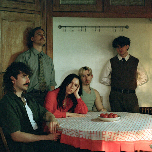 Le groupe post punk Dog Race assis autour d’une table en intérieur, ambiance vintage