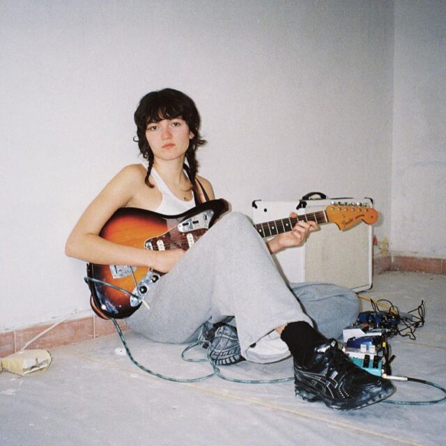 Billie, artiste indie pop / new wave, assise au sol avec une guitare électrique